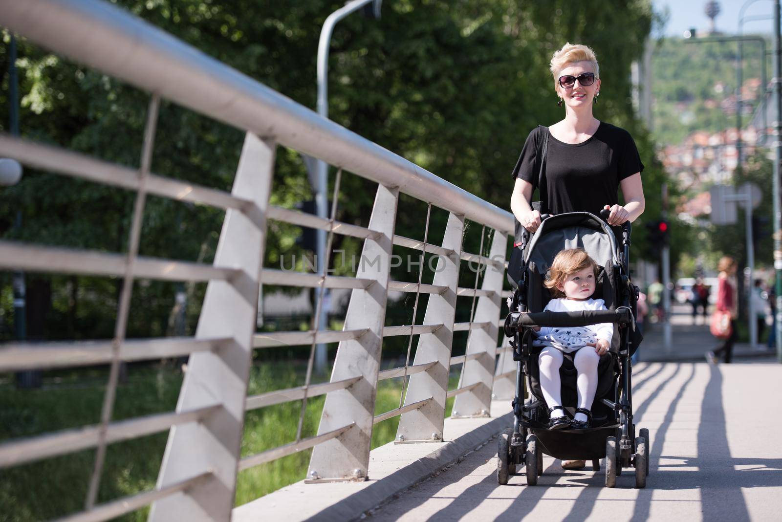 beautiful young mother with blond hair and sunglasses pushed her baby daughter in a stroller on a summer day