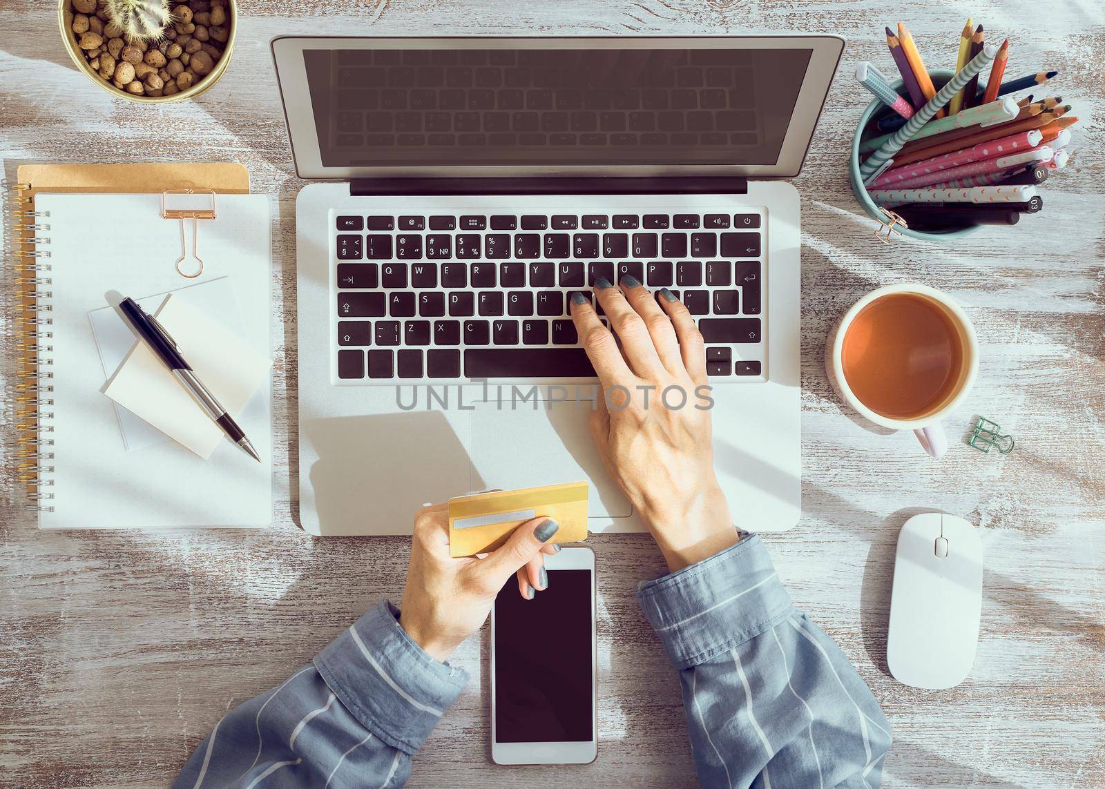 Online shopping concept. Unrecognizable woman drinking tea and looking at laptop, top view faceless person pay for purchases by credit card