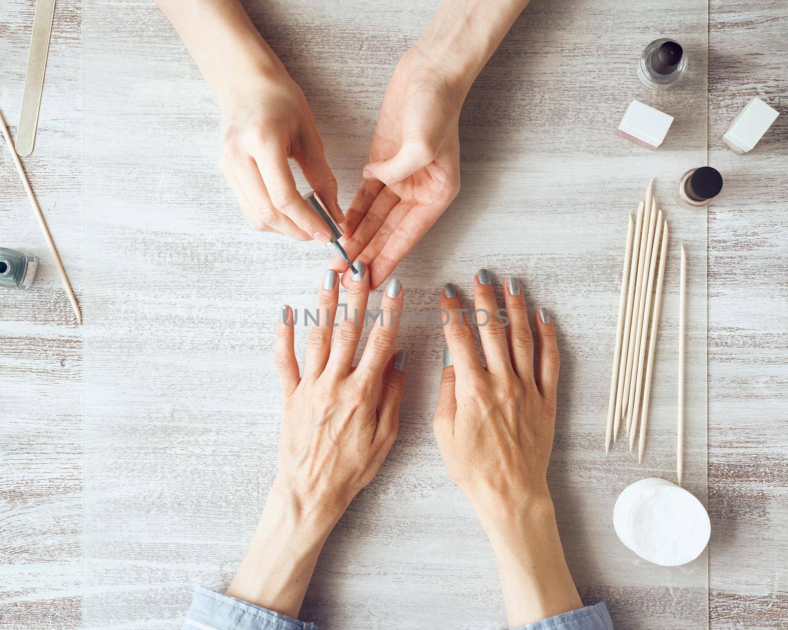 Mother and daughter do manicure, paint nails with varnish. Home care during quarantine, self-isolation. Top view of hands on table.