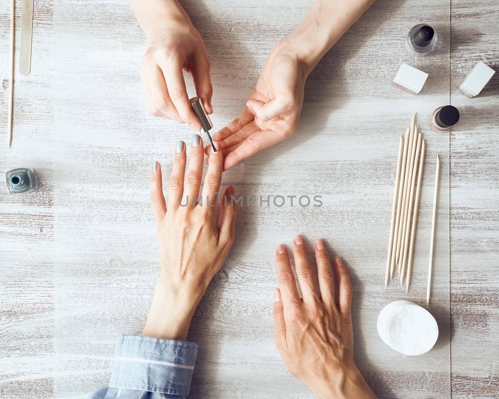 Mother and daughter do manicure, paint nails with varnish. Home care during quarantine, self-isolation. Top view of hands on table.