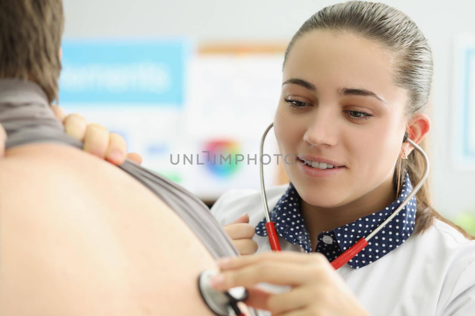 Young female doctor listen to patients back with stethoscope equipment by kuprevich