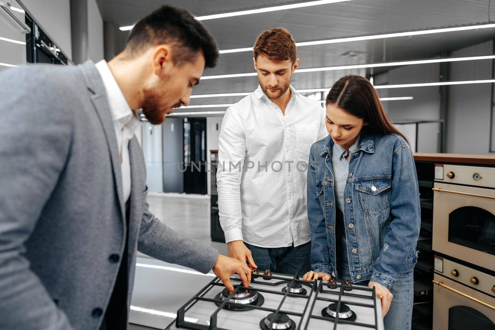 Male shop assistant helps young couple to choose new home appliance in hypermarket