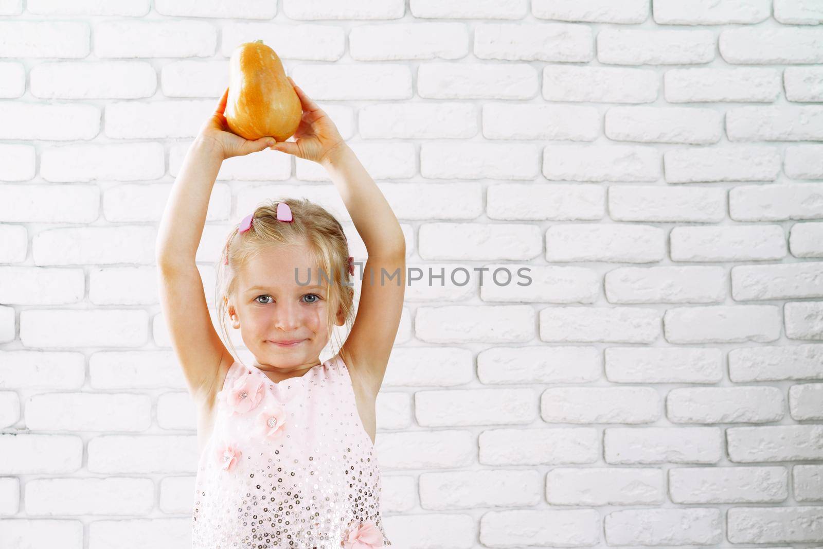 Cute little girl in pink dress holding pumpkin in her hands by Fabrikasimf