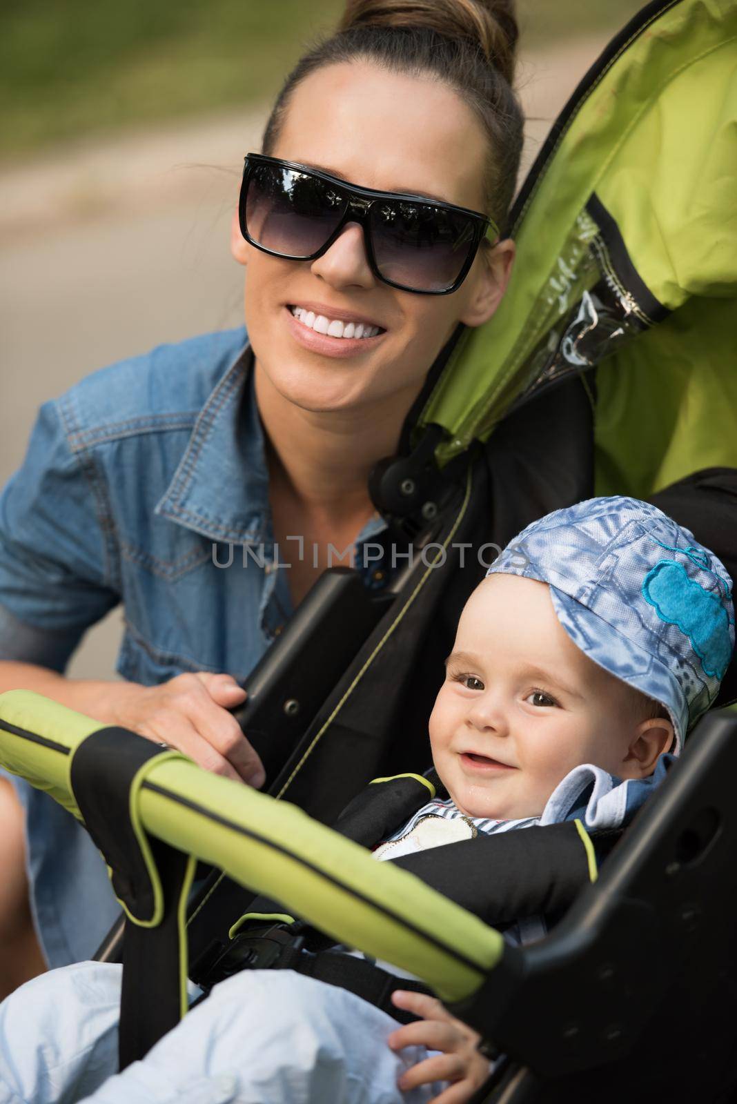 portrait of a beautiful young mother with sunglasses and a baby in a stroller on a sunny day in the park