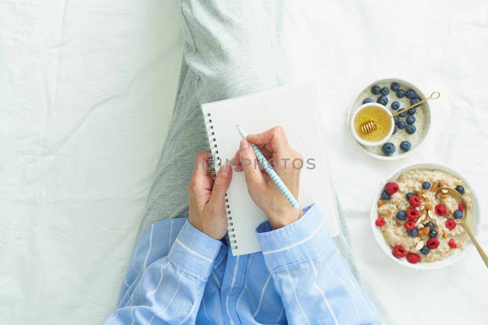 woman writes in large white open notebook, lay on bed with breakfast with oatmeal, top view, copy space.
