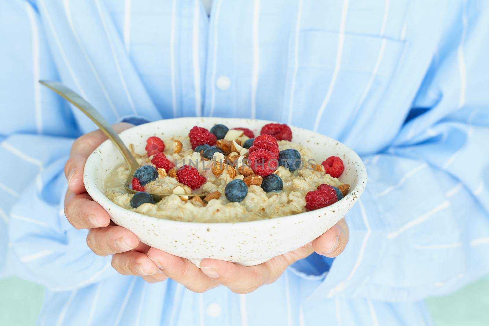 Faceless woman holds in hands breakfast, oatmeal porridge with berries and nuts, healthy food, proper nutrition. Sunshine, early morning, quiet home environment. Side view