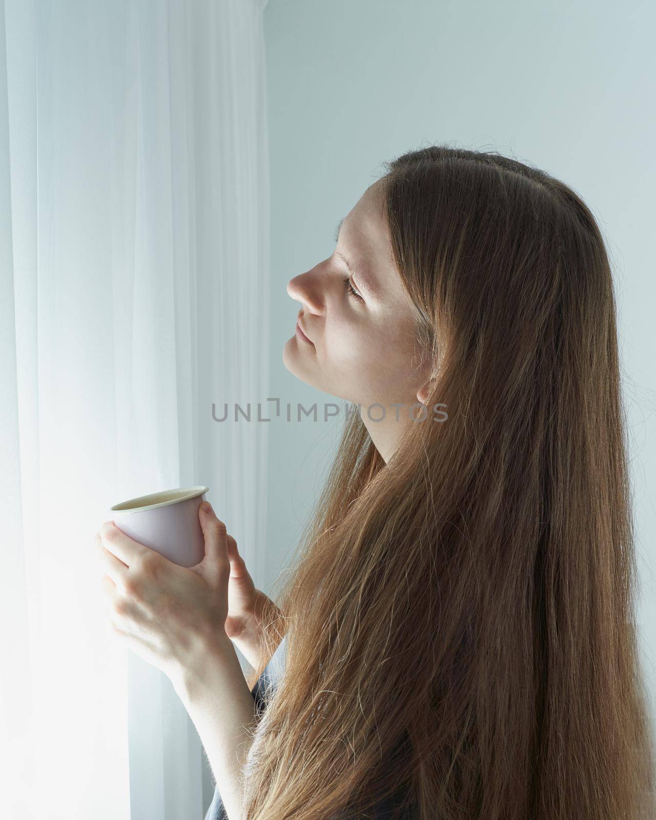 Social media, digital detox. Quarantine, self-isolation, sociophobia. Beautiful girl thoughtfully looks out window. Woman with long hair is deep in thought.