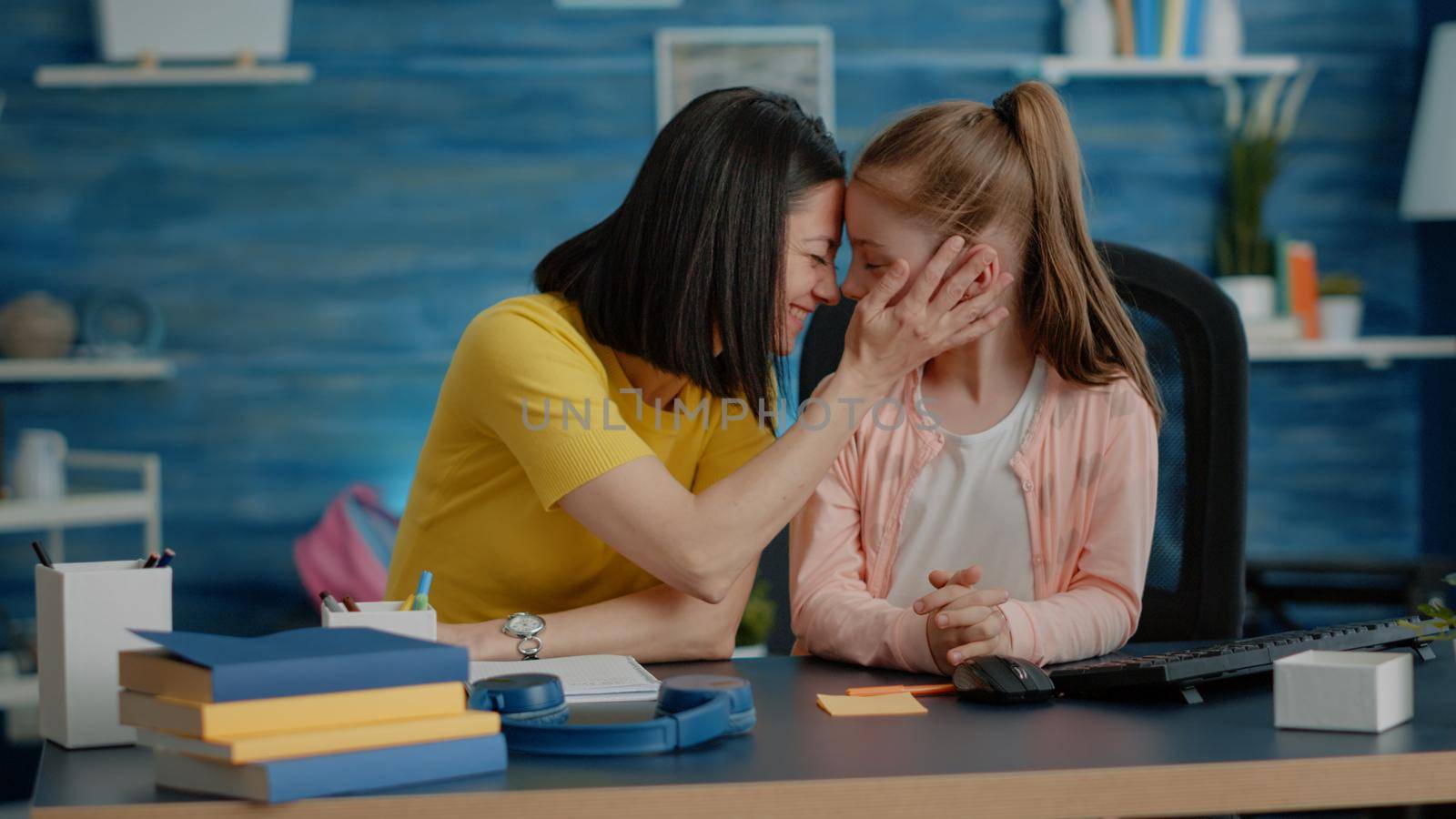 Little girl and mother preparing for online school courses, sitting at desk. Affectionate parent giving assistance and support to young child with remote class lessons and tasks for education.