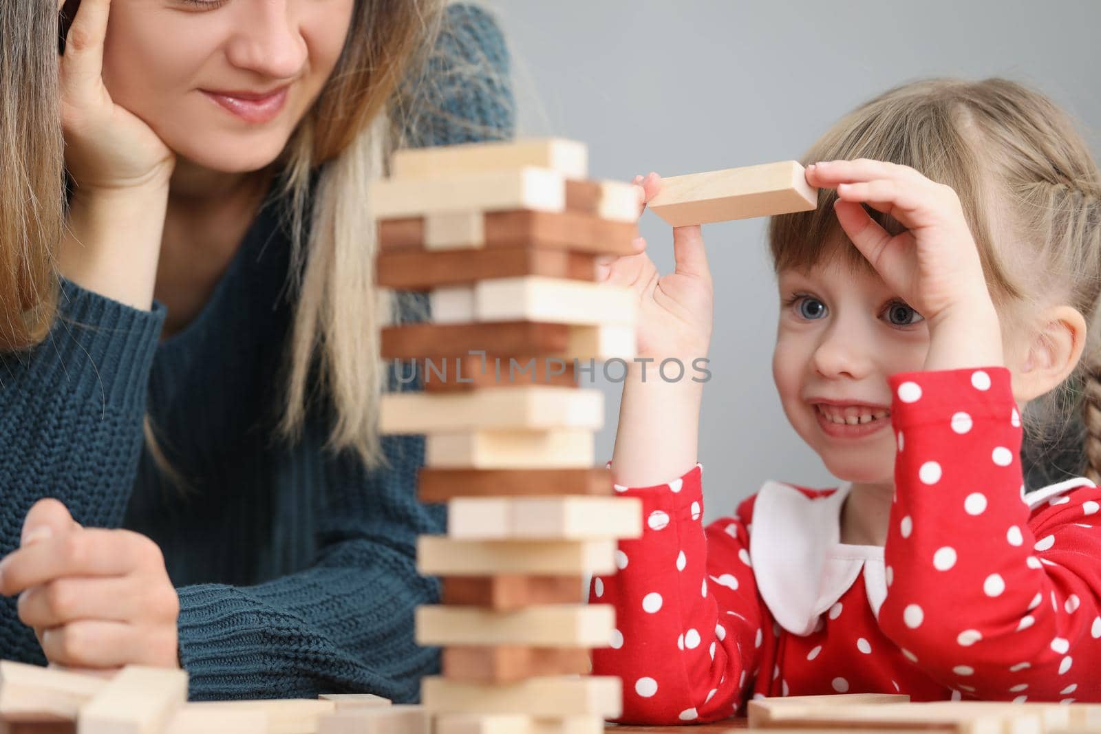 Pretty little kid pulling wooden block out of tower and smile by kuprevich