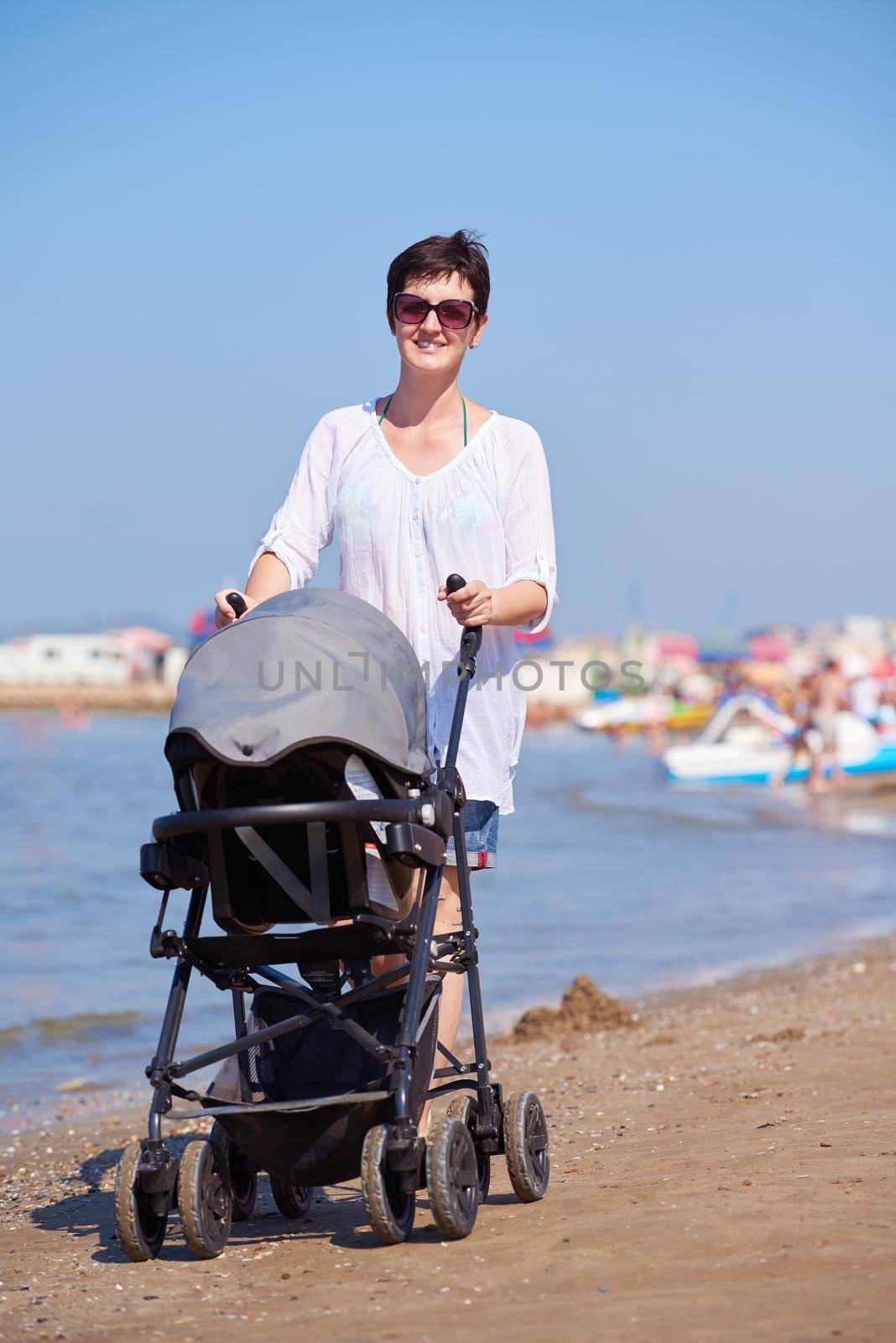 happy young mother walking on beach and push baby carriage