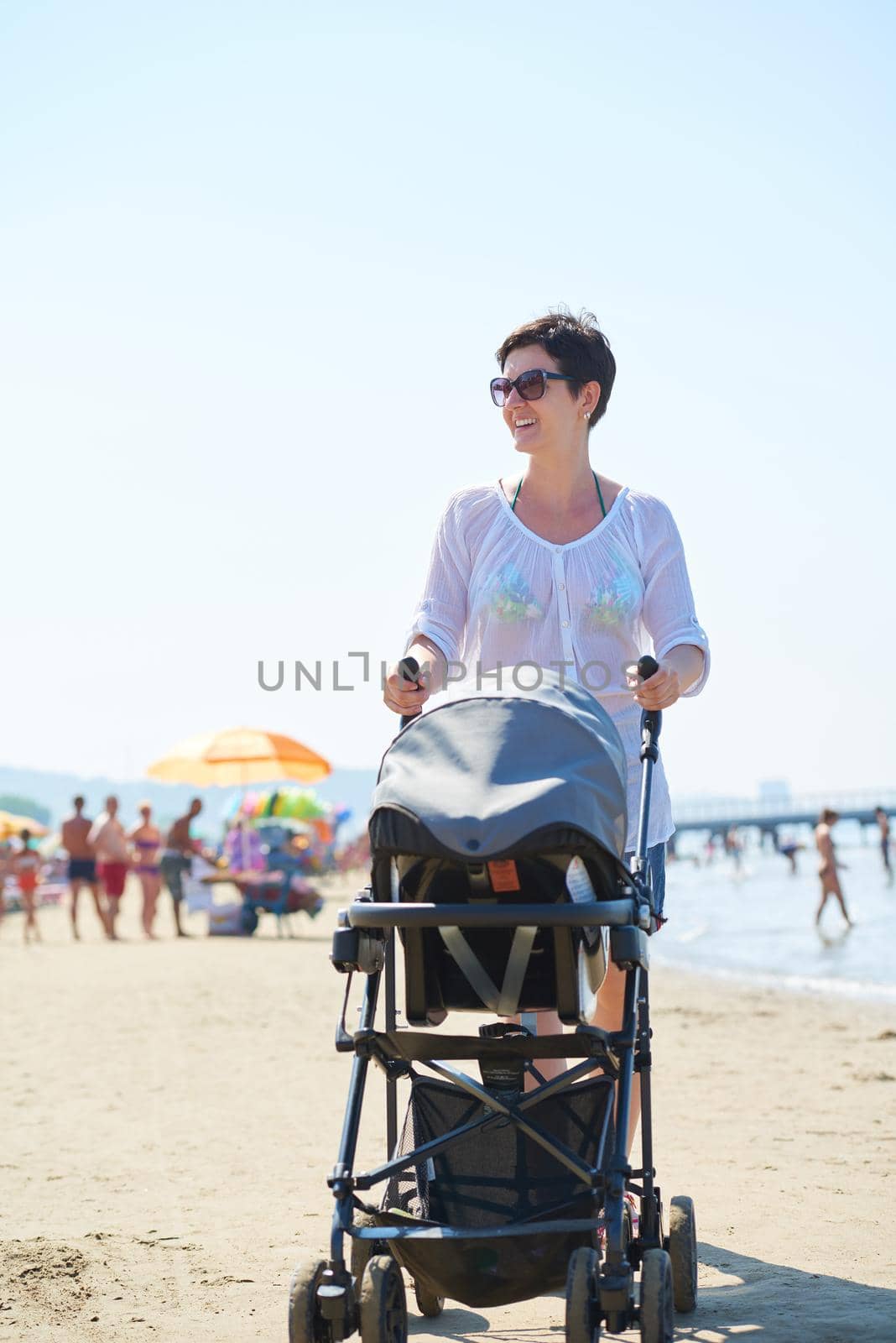 happy young mother walking on beach and push baby carriage