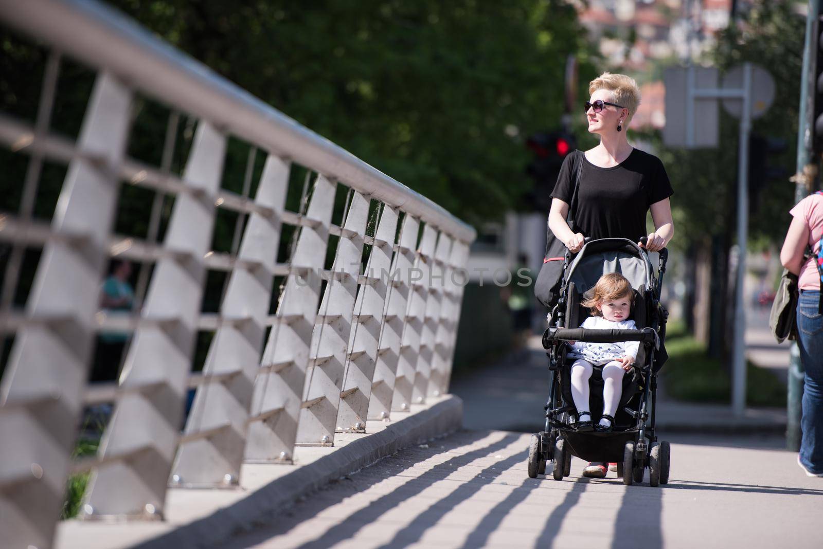 beautiful young mother with blond hair and sunglasses pushed her baby daughter in a stroller on a summer day
