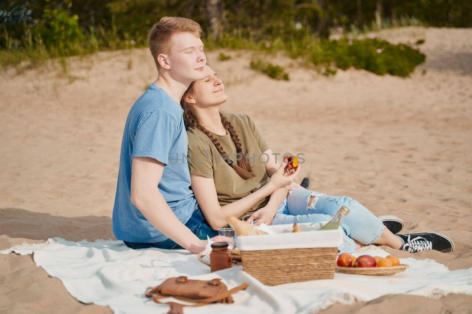 Picnic on beach with food and drinks. Young boy and girl sunbathing, sitting on sand. Teens couple. Sunny summer day, rest.