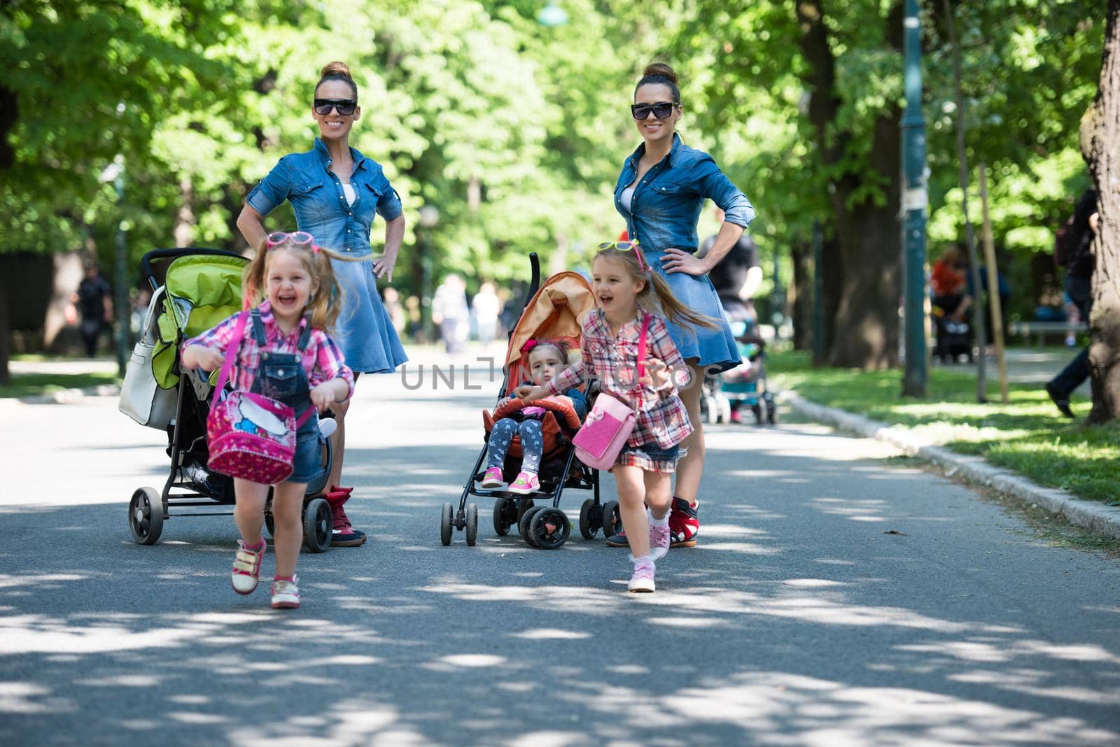 Young beautiful twins mother with children enjoying a sunny day in city park