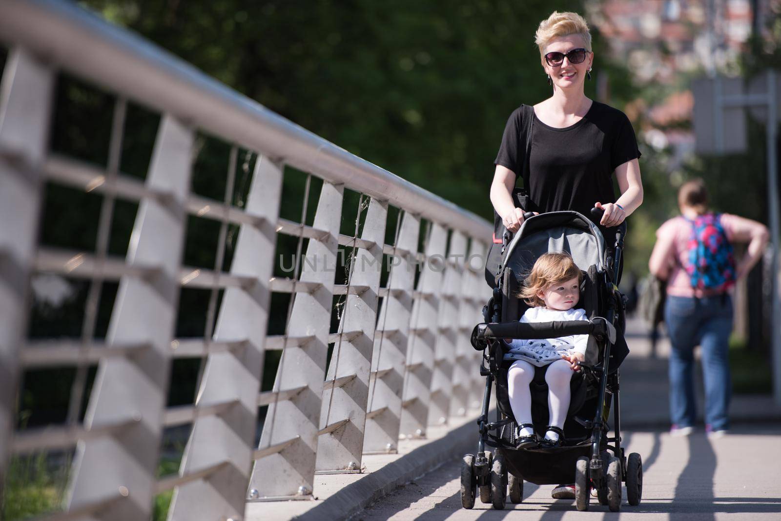 beautiful young mother with blond hair and sunglasses pushed her baby daughter in a stroller on a summer day