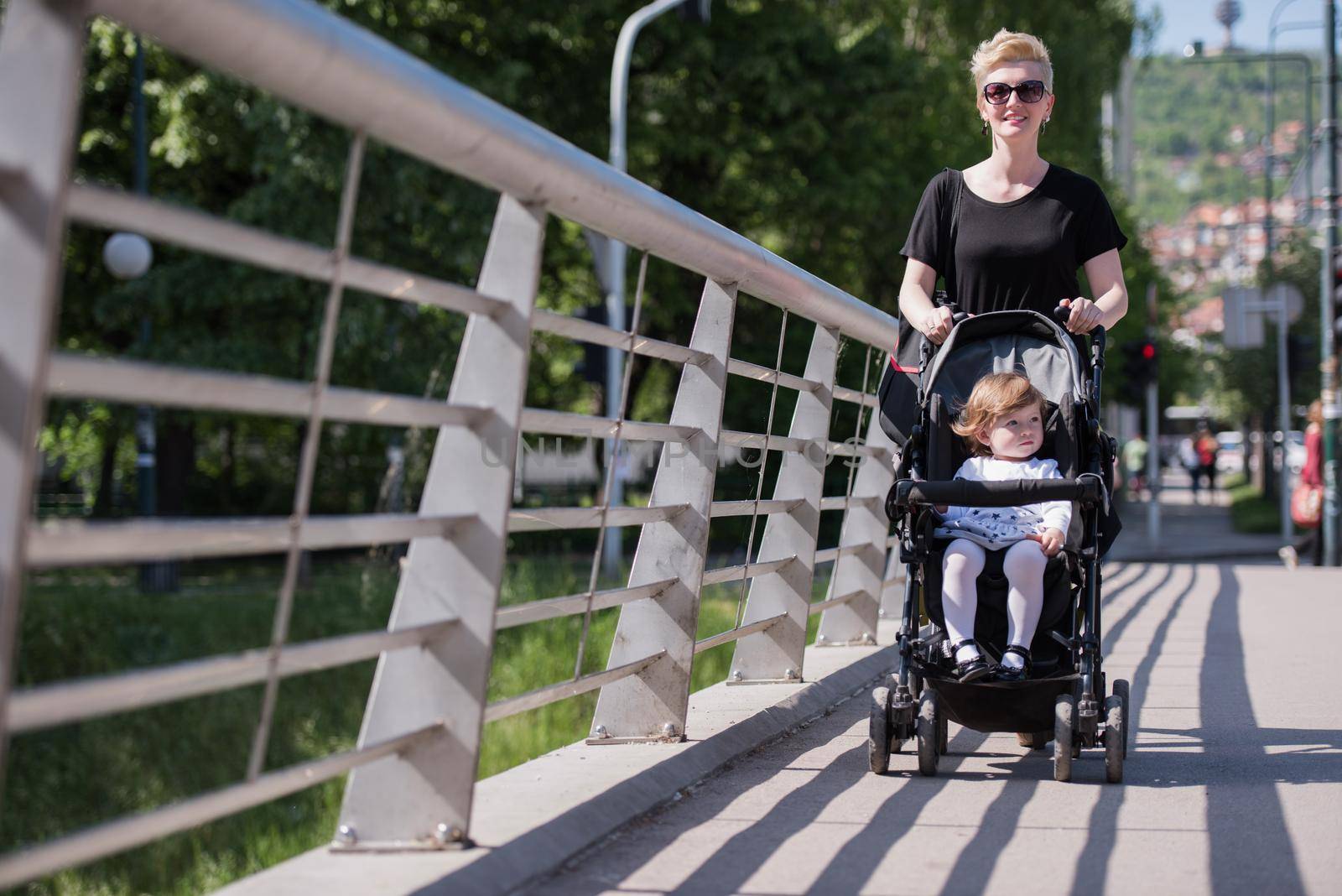 beautiful young mother with blond hair and sunglasses pushed her baby daughter in a stroller on a summer day