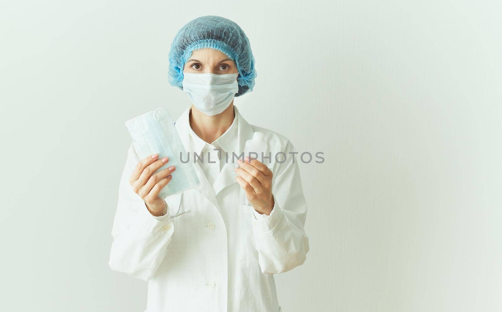 Female doctor in medical mask and uniform offers mask and disinfectant in bottle to prevent from coronavirus. Covid-19 protection, medical information. Copy space