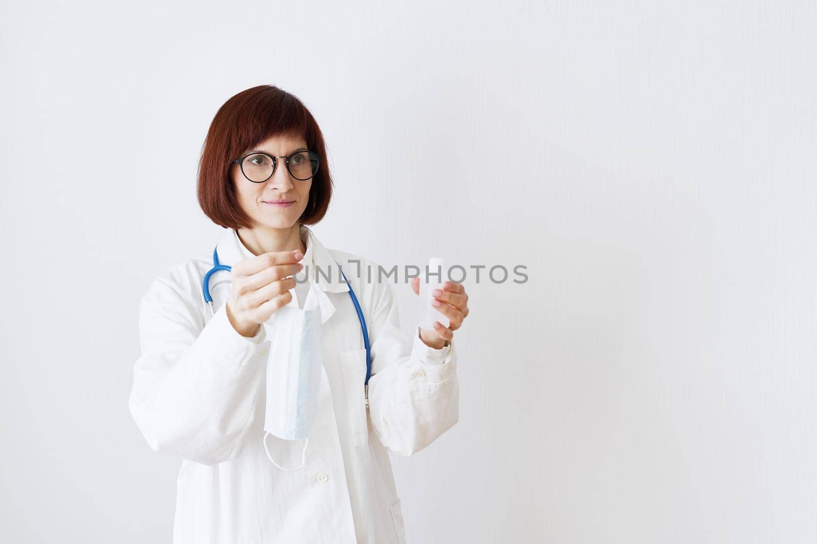 Female doctor in medical mask and uniform offers mask and disinfectant in bottle by NataBene