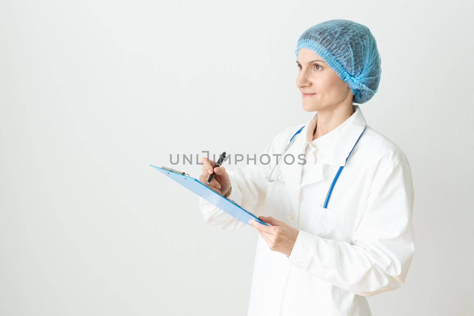 Female adult doctor stands on white background. Beautiful woman, thinking, smiling, writing. by NataBene
