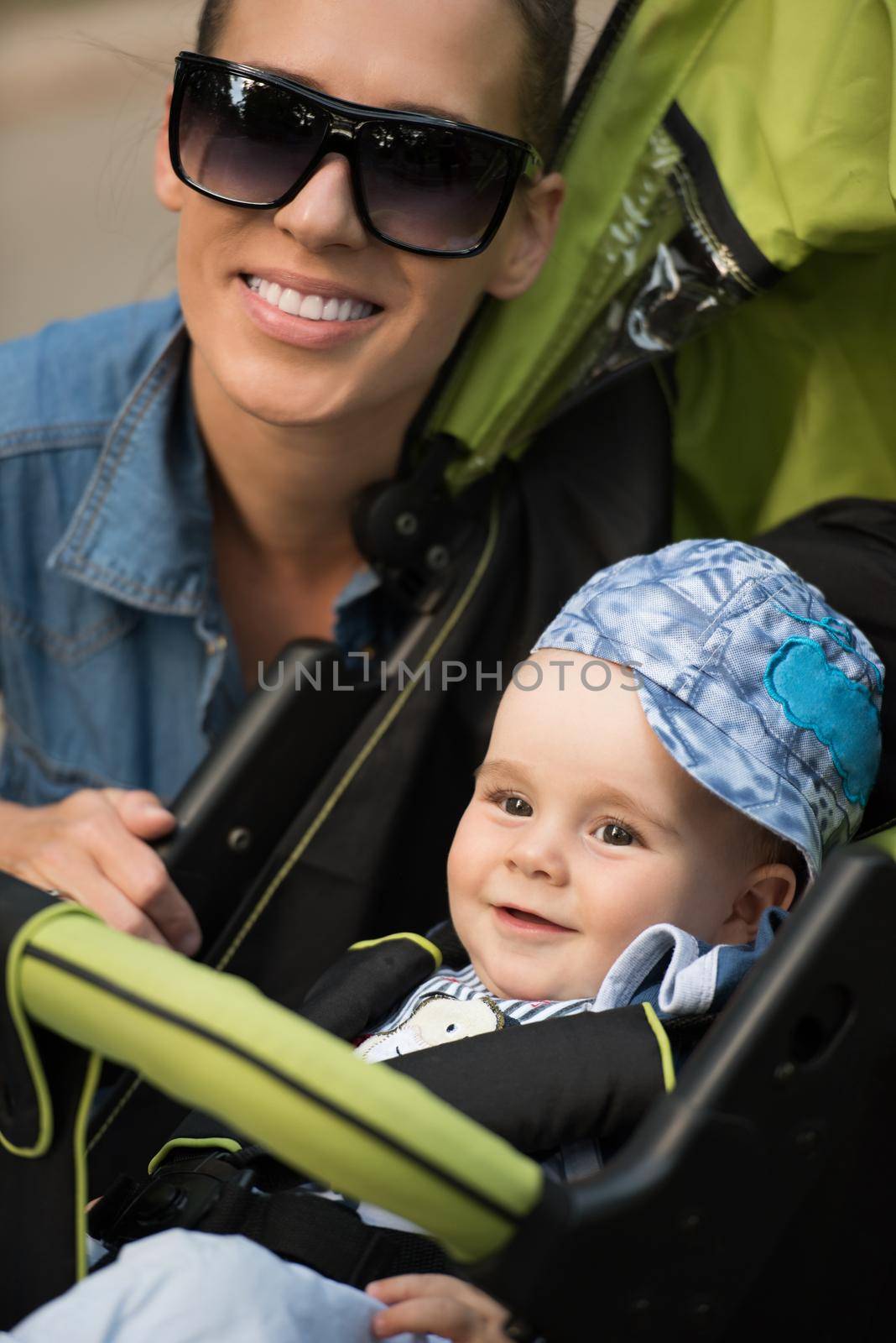 portrait of a beautiful young mother with sunglasses and a baby in a stroller on a sunny day in the park