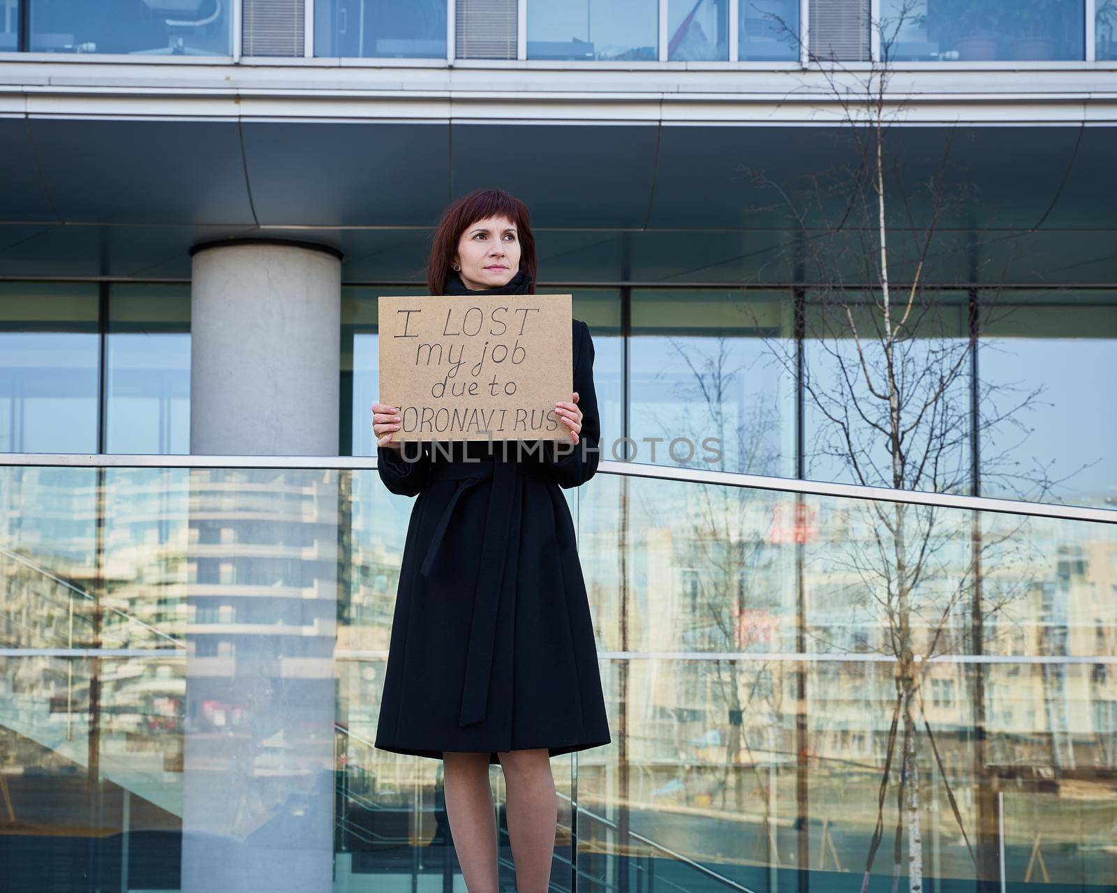 Woman holds sign saying I lost my job because of coronavirus. Concept of job loss due to the COVID-19 virus pandemic. Female stands against background of business center
