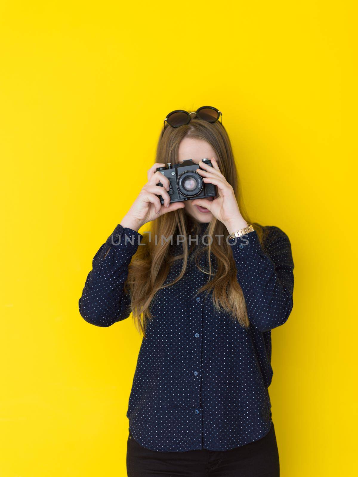 portrait of a smiling pretty girl taking photo on a retro camera isolated over yellow background