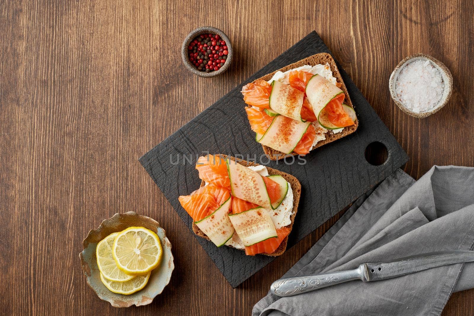 Smorrebrod - traditional Danish sandwiches. Black rye bread with salmon, cream cheese, cucumber on dark brown wooden background