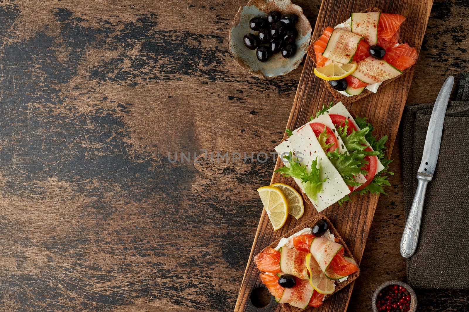 Smorrebrod - traditional Danish sandwiches. Black rye bread with salmon, cream cheese, cucumber, tomatoes on dark brown wooden background, copy space