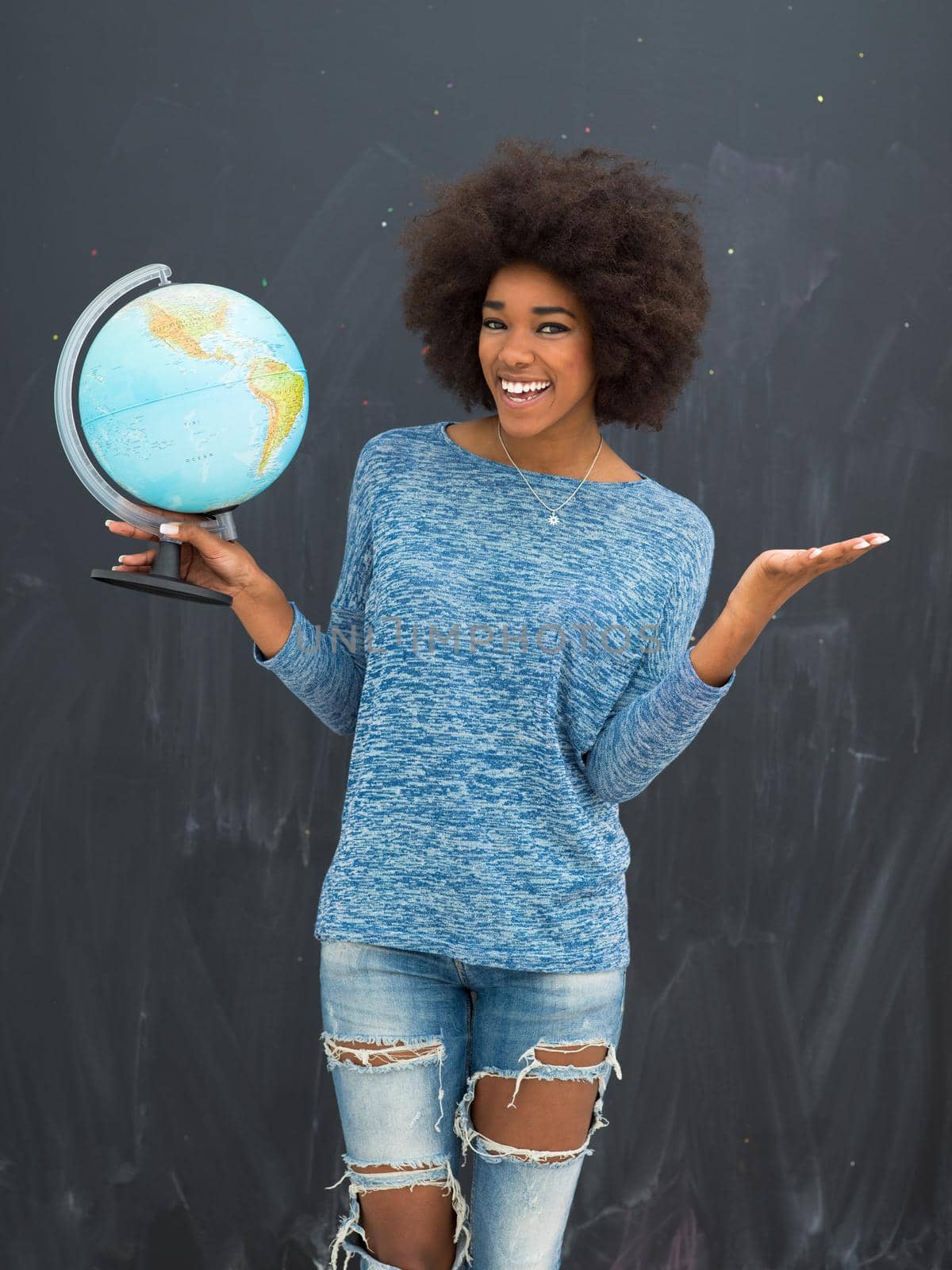 portrait of a beautiful friendly African American woman with a curly afro hairstyle and lovely smile holding Globe of the world isolated on a gray background