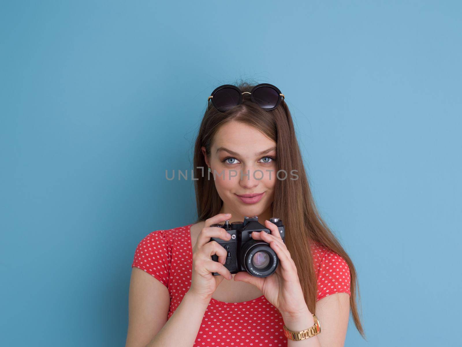 portrait of a smiling pretty girl taking photo on a retro camera isolated over blue background