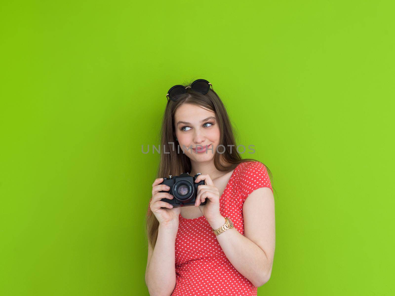 portrait of a smiling pretty girl taking photo on a retro camera isolated over green background