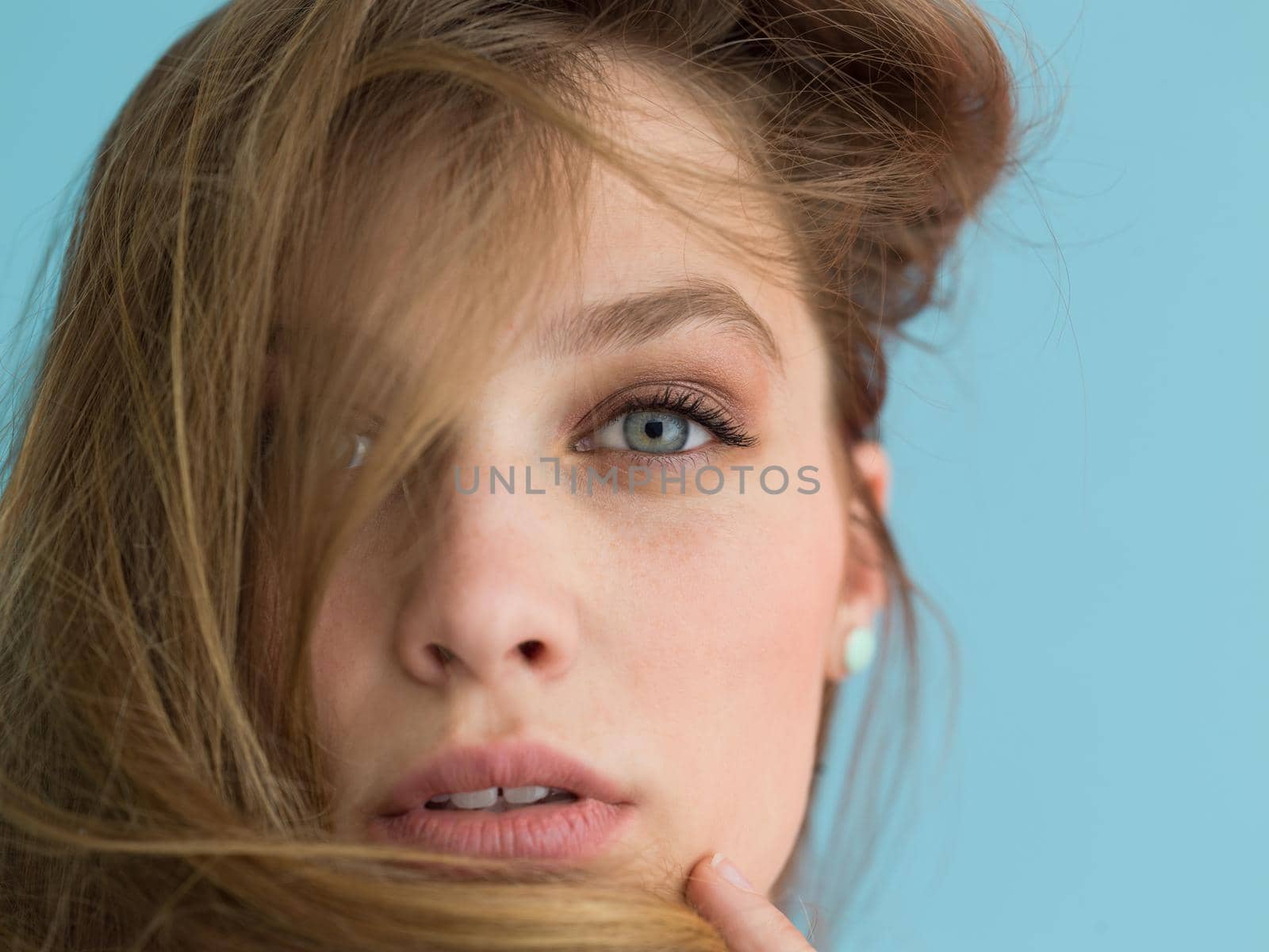 Portrait of a beautiful positive young woman while playing with her long silky hair isolated on blue background
