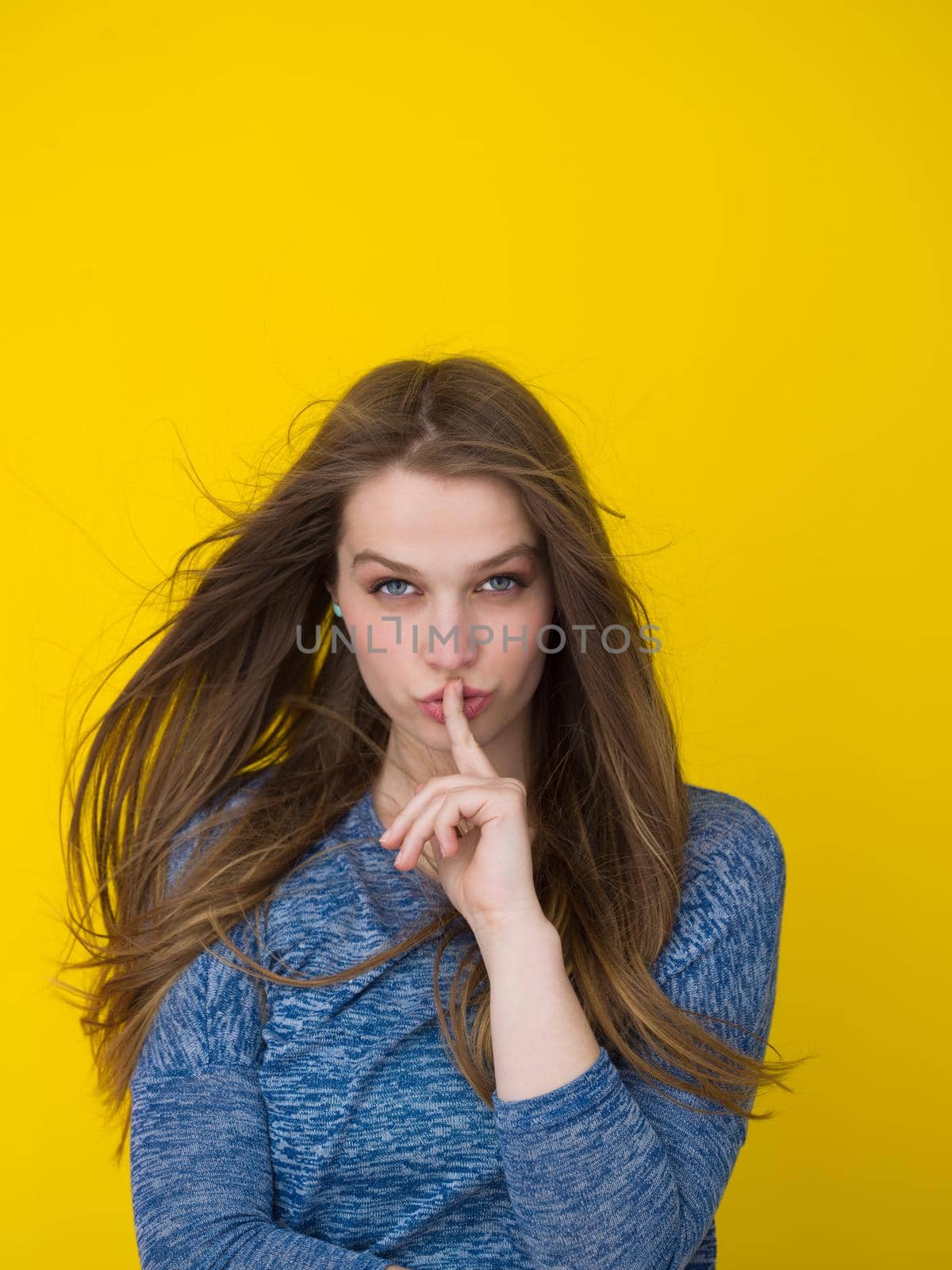 Portrait of a beautiful positive young woman while playing with her long silky hair isolated on yellow background