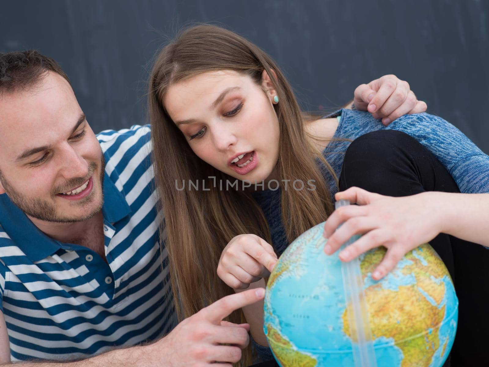 Young lovely couple in casual clothing investigating globe isolated over gray background