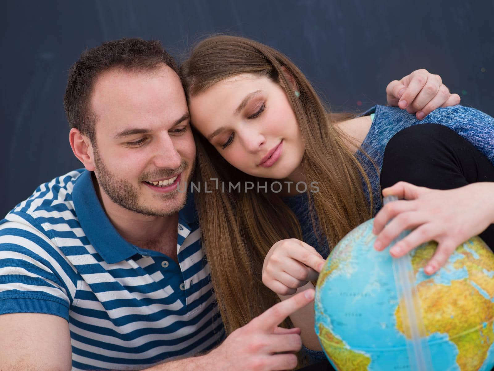 Young lovely couple in casual clothing investigating globe isolated over gray background