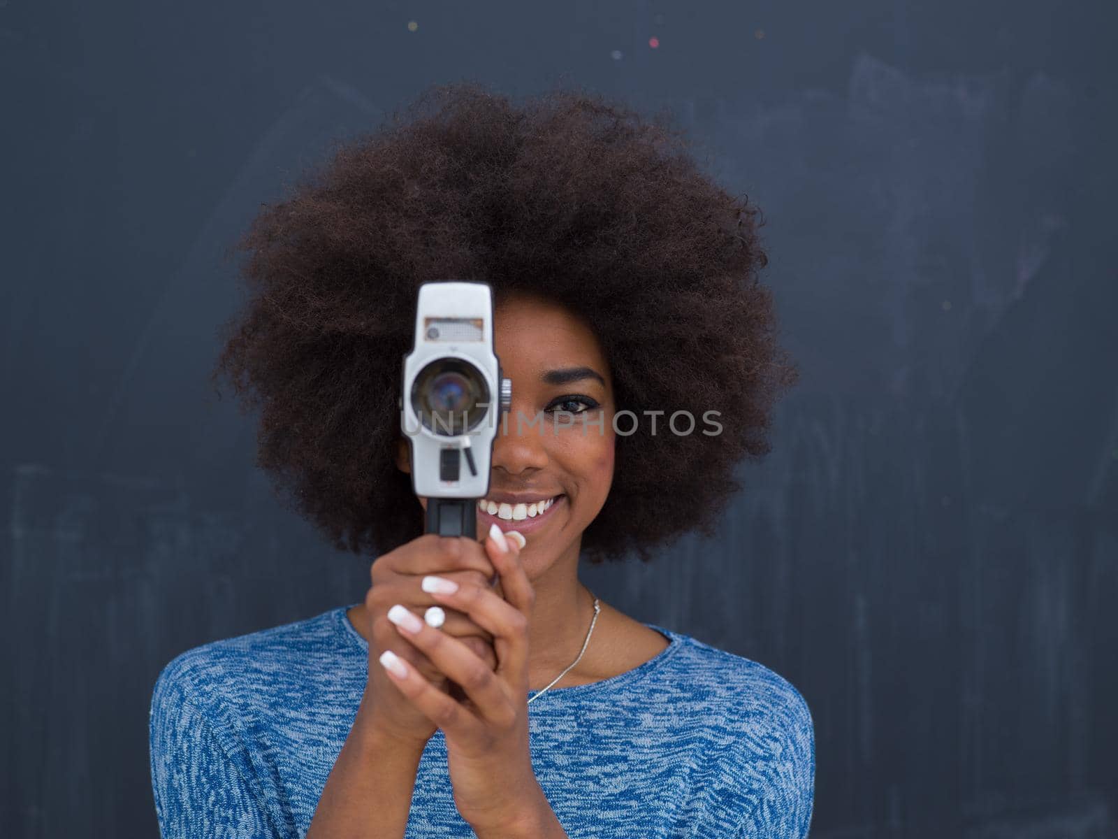 A young beautiful african american woman using a retro video camera isolated on a gray background