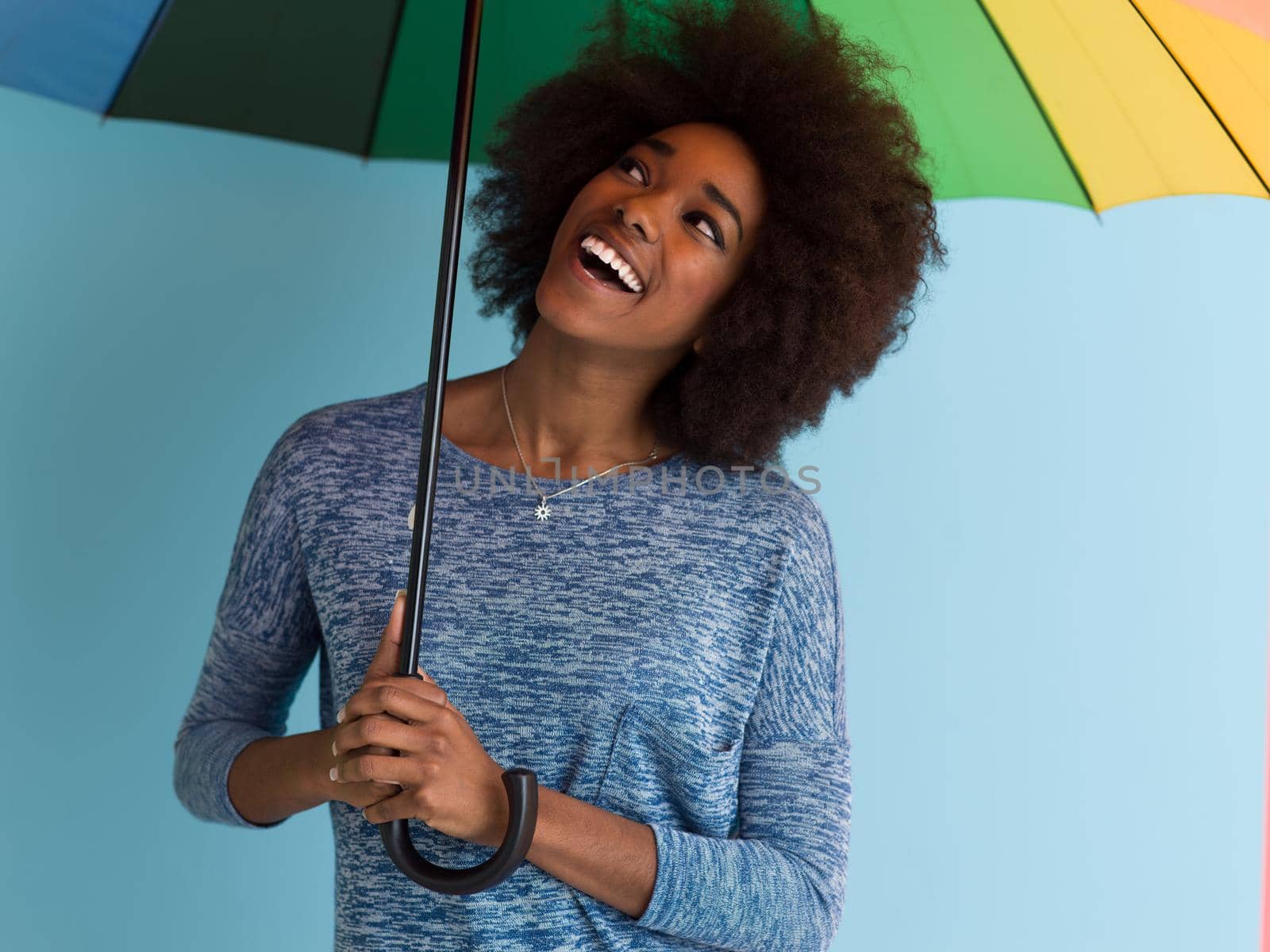 Portrait of young beautiful african american woman holding a colorful umbrella isolated on a Blue background