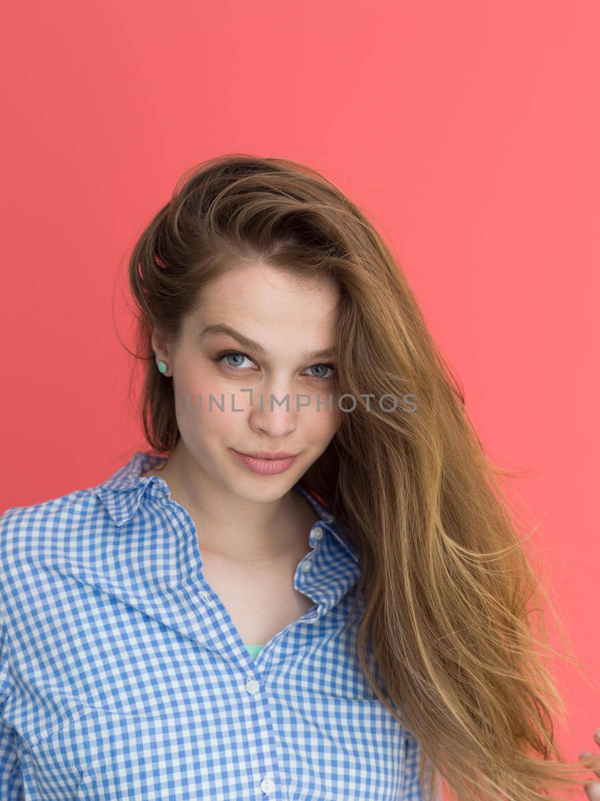Portrait of a beautiful positive young woman while playing with her long silky hair isolated on red background