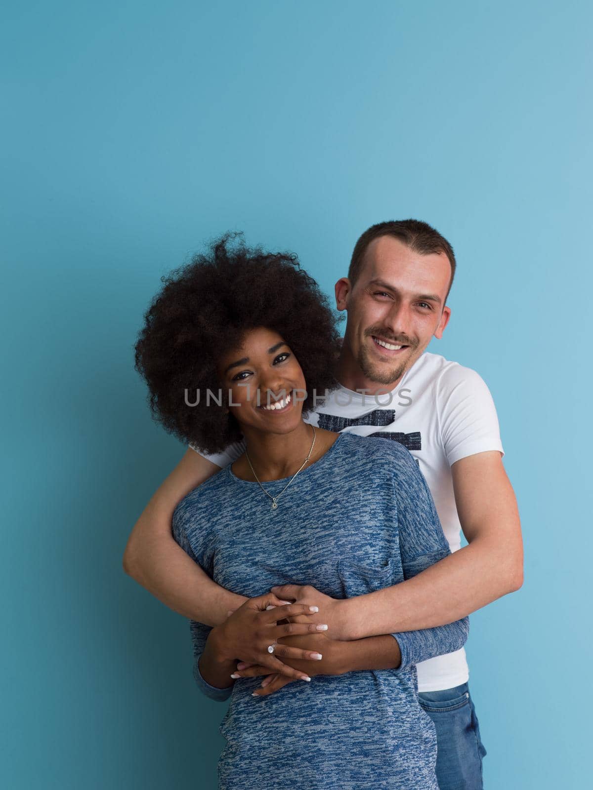 Young happy multiethnic couple laughing and hugging isolated on a blue background
