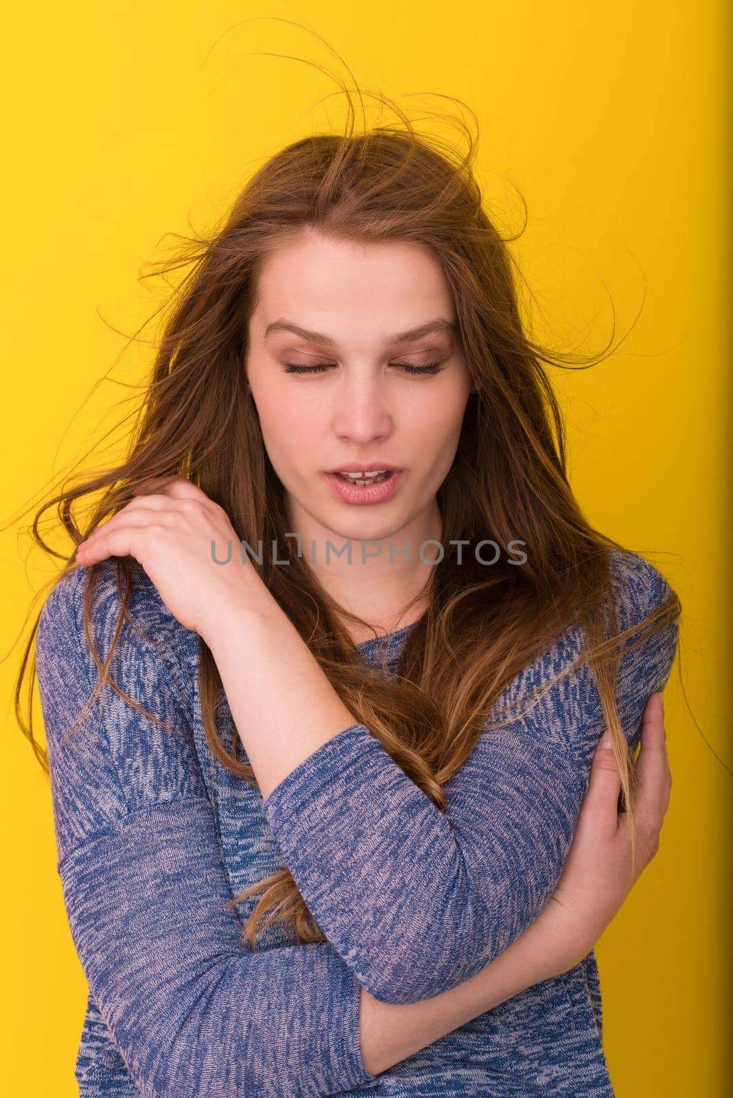 Portrait of a beautiful positive young woman while playing with her long silky hair isolated on yellow background