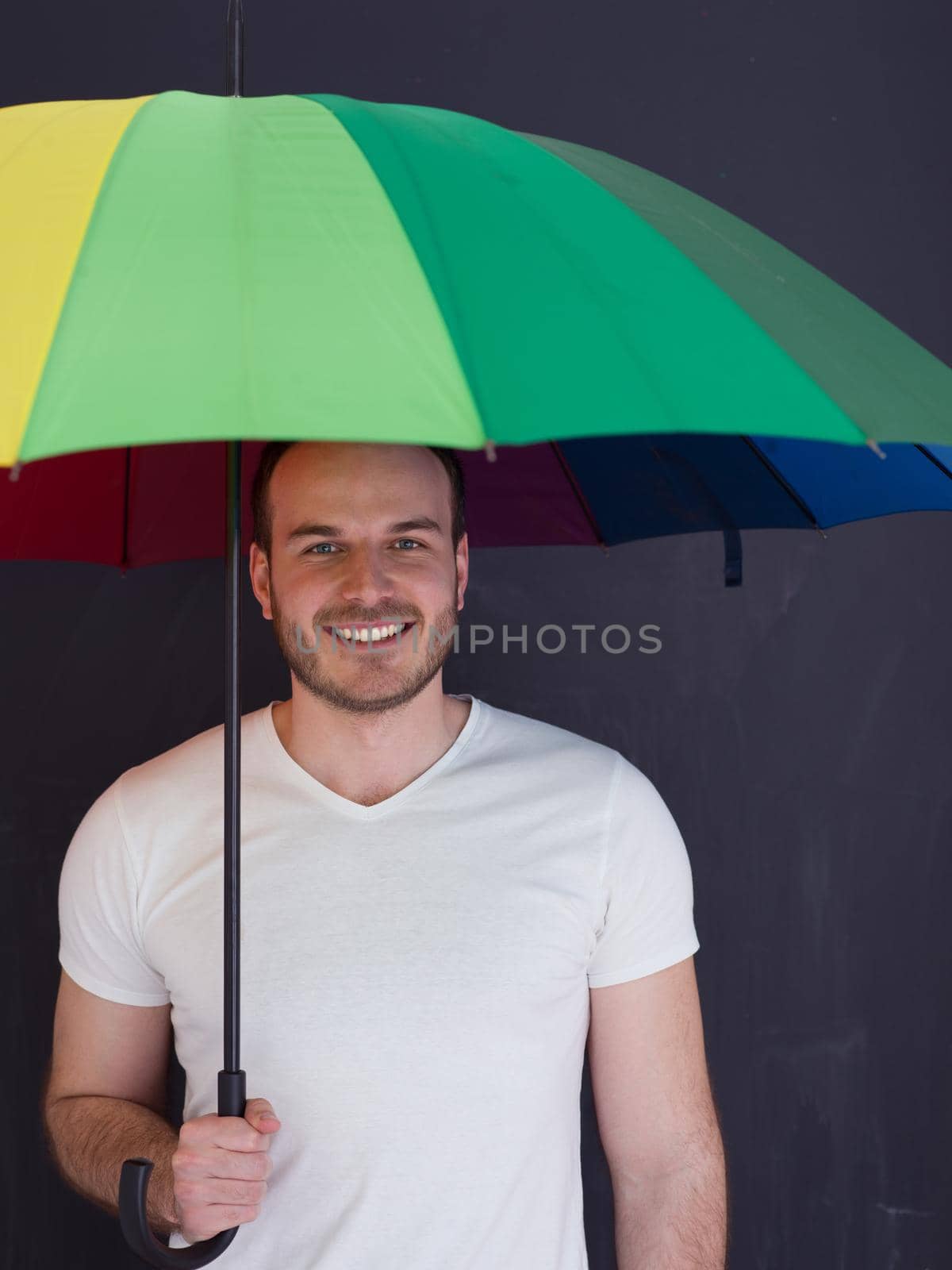 portrait of a young handsome man with a colorful umbrella isolated on a gray background
