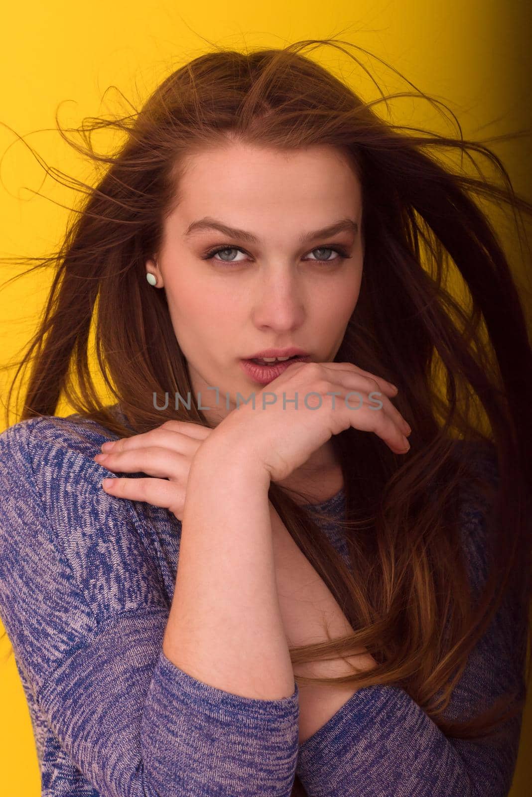 Portrait of a beautiful positive young woman while playing with her long silky hair isolated on yellow background