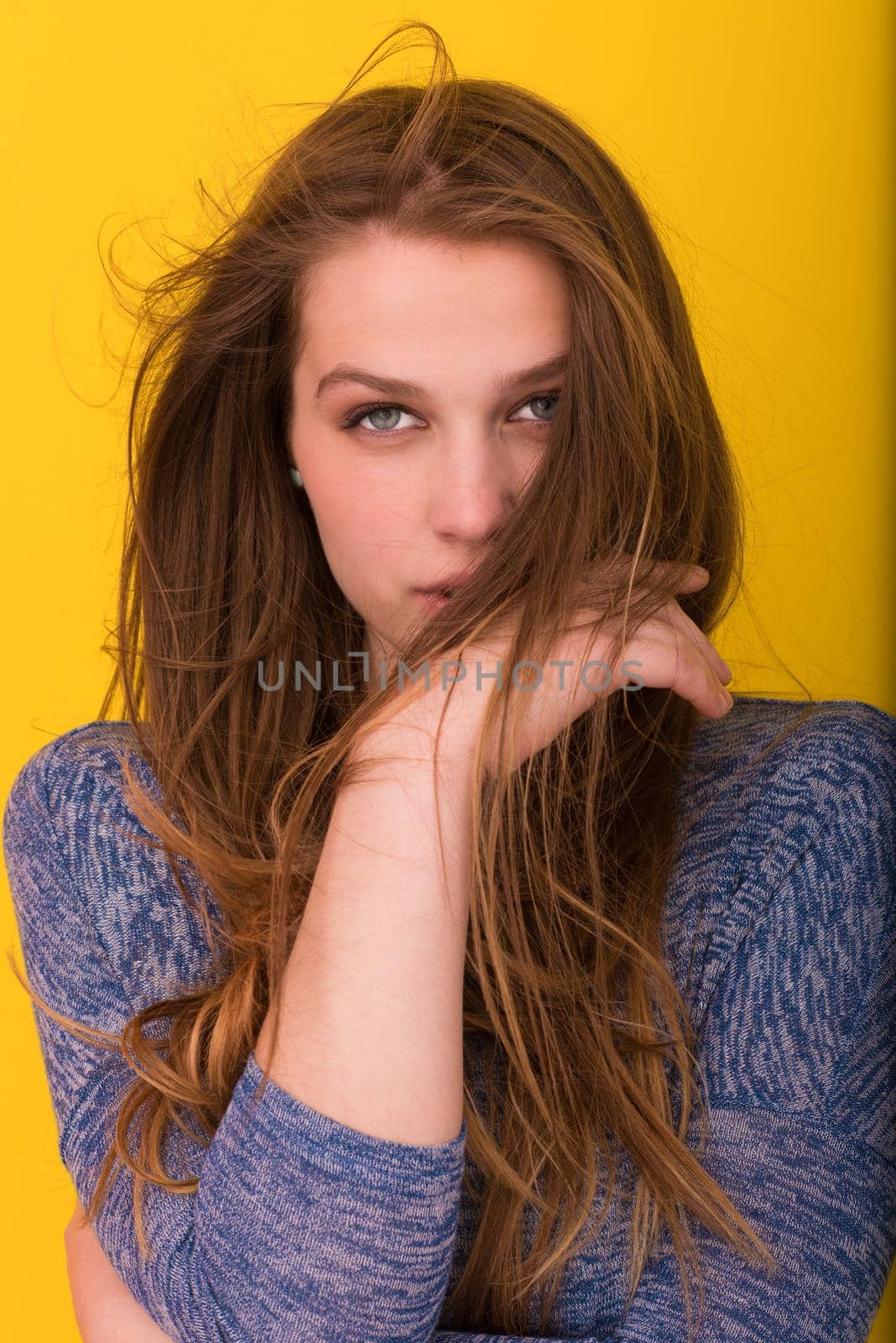 Portrait of a beautiful positive young woman while playing with her long silky hair isolated on yellow background