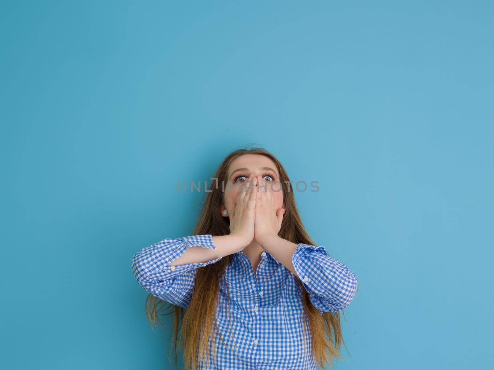Portrait of a beautiful positive young woman while playing with her long silky hair isolated on blue background