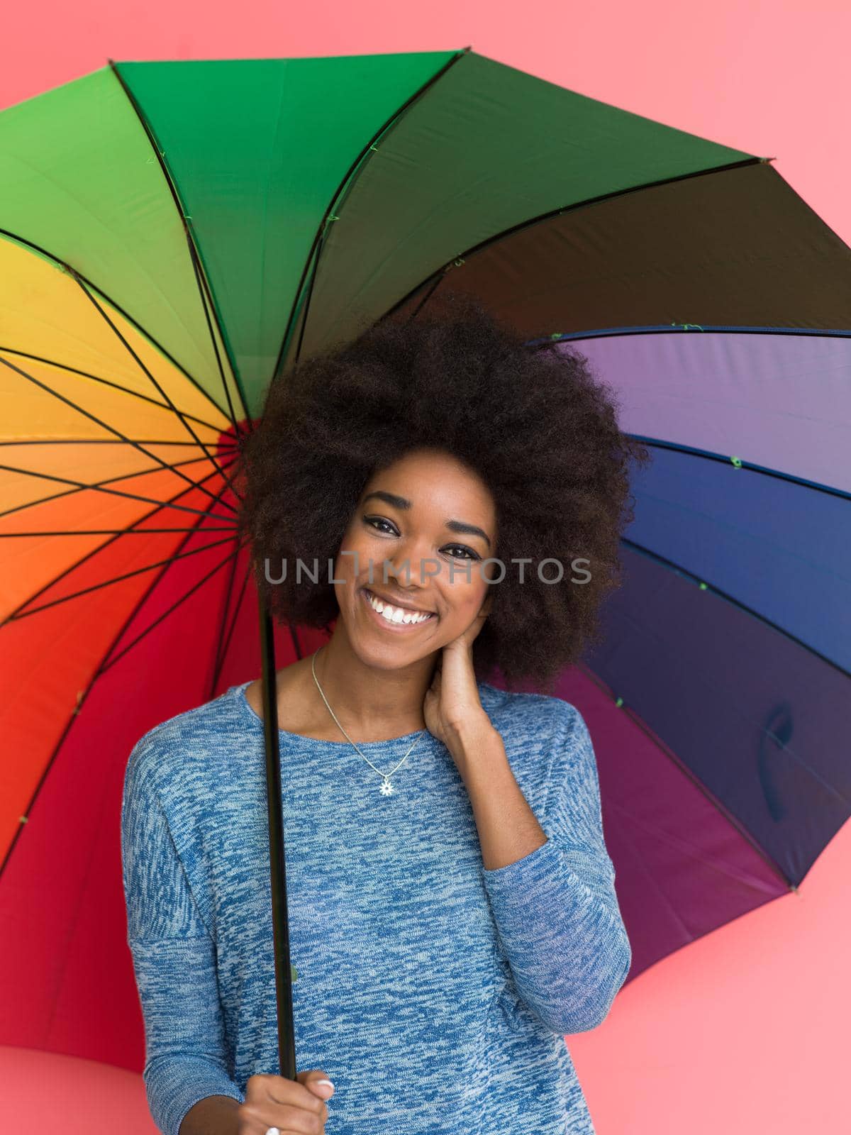 Portrait of young beautiful african american woman holding a colorful umbrella isolated on a Pink background