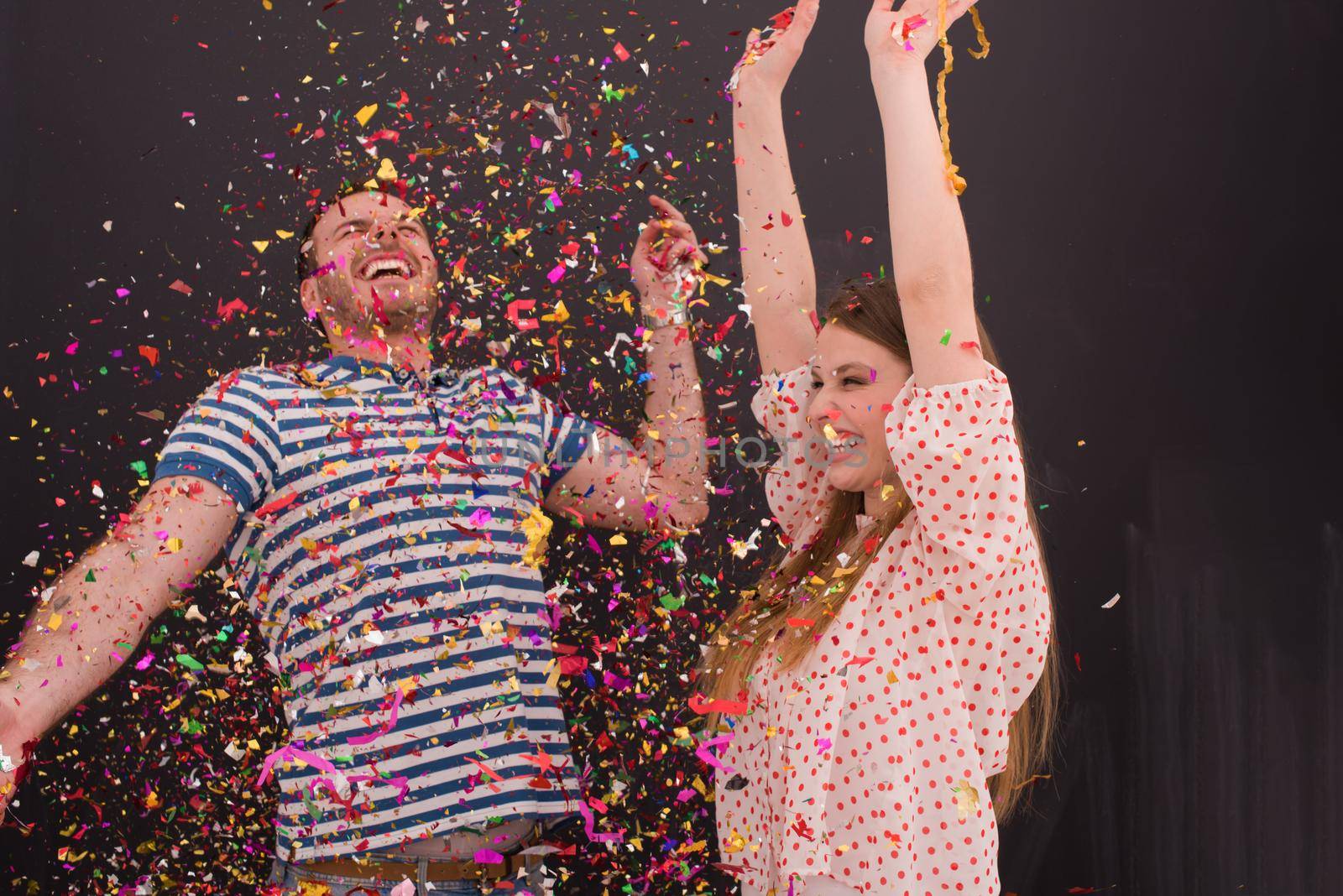 handsome young couple celebrating new year and chrismas party while blowing confetti decorations to camera isolated over gray background