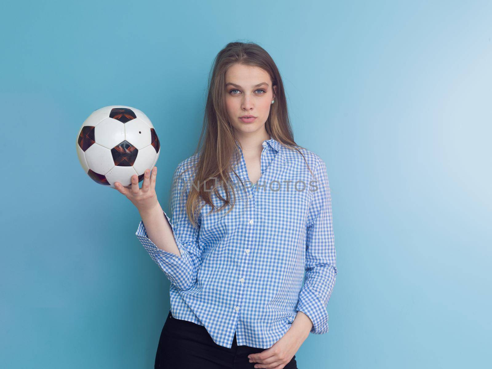 Portrait of a beautiful positive young woman while playing with a soccer ball isolated on blue background