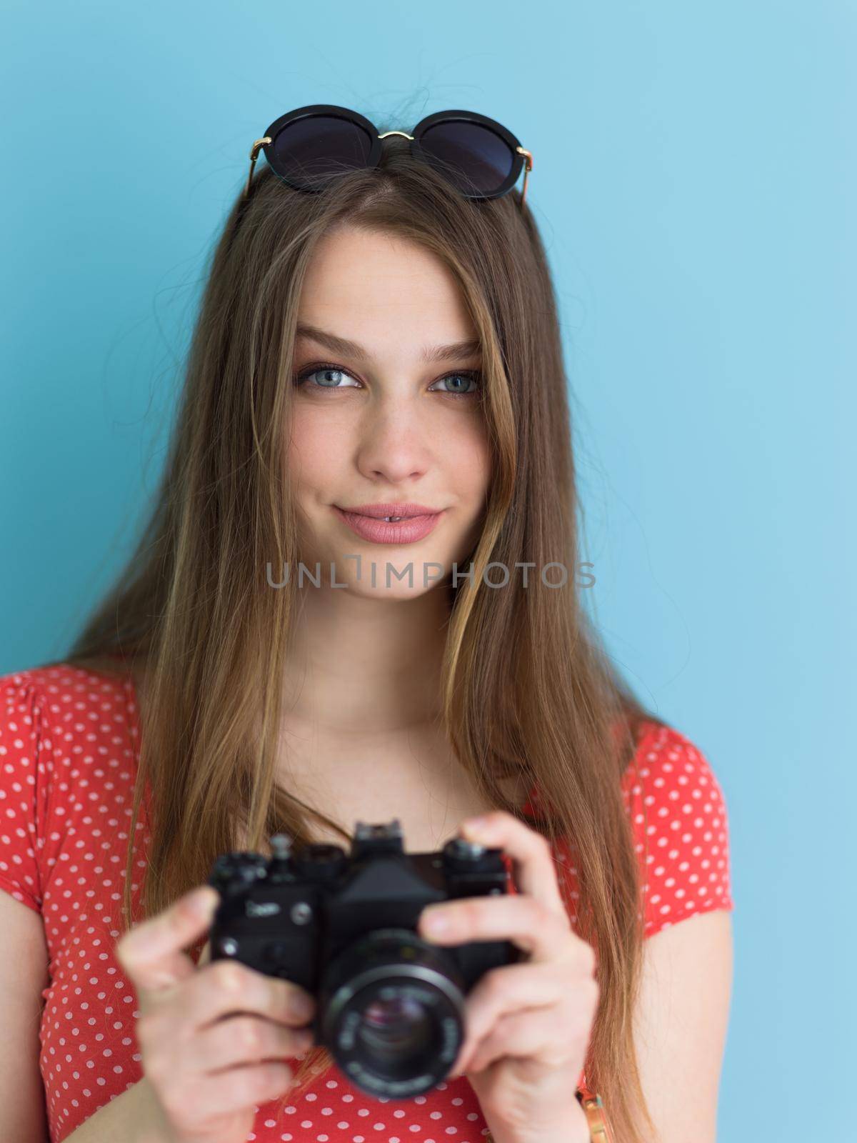 portrait of a smiling pretty girl taking photo on a retro camera isolated over blue background