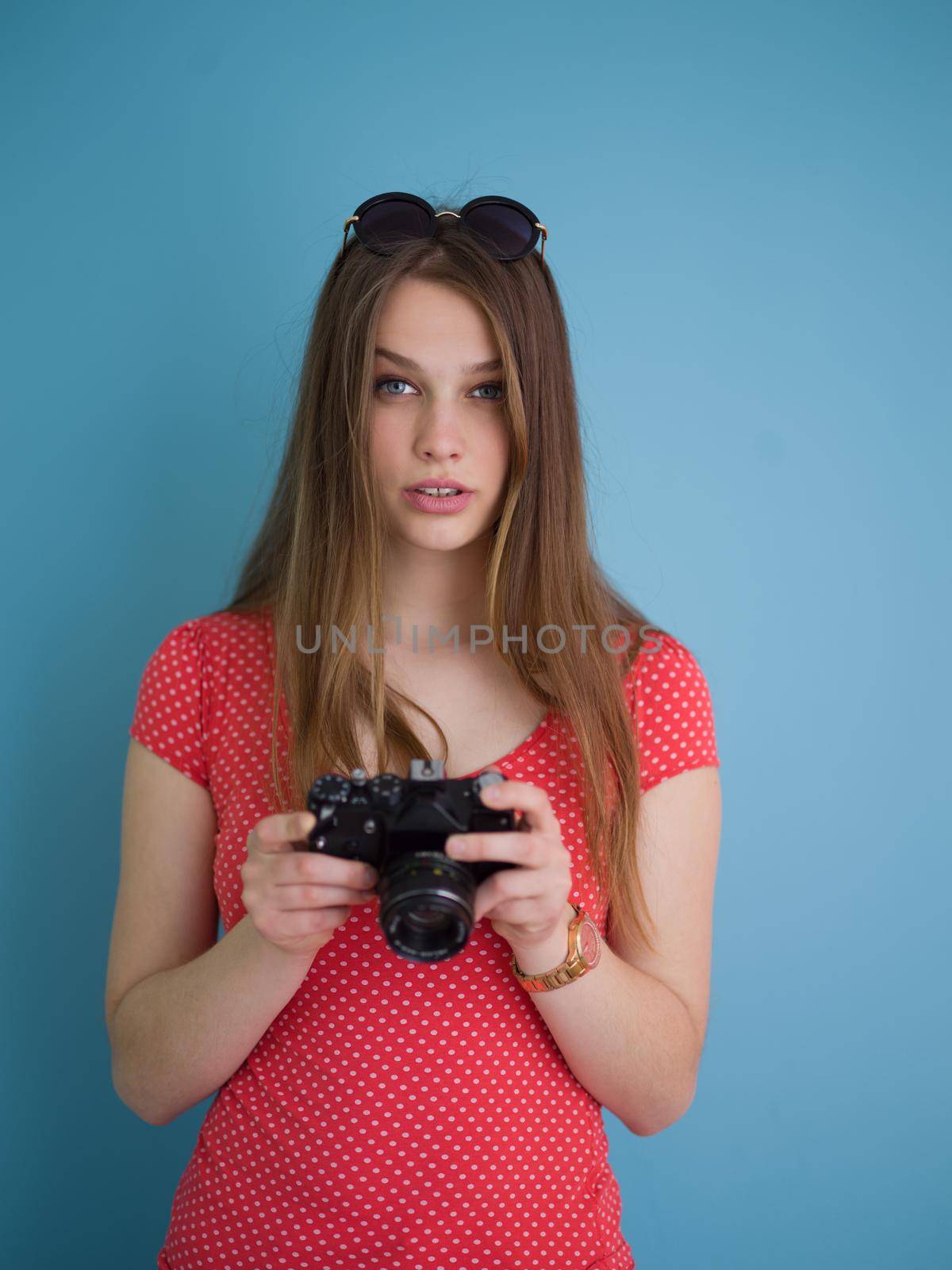 portrait of a smiling pretty girl taking photo on a retro camera isolated over blue background