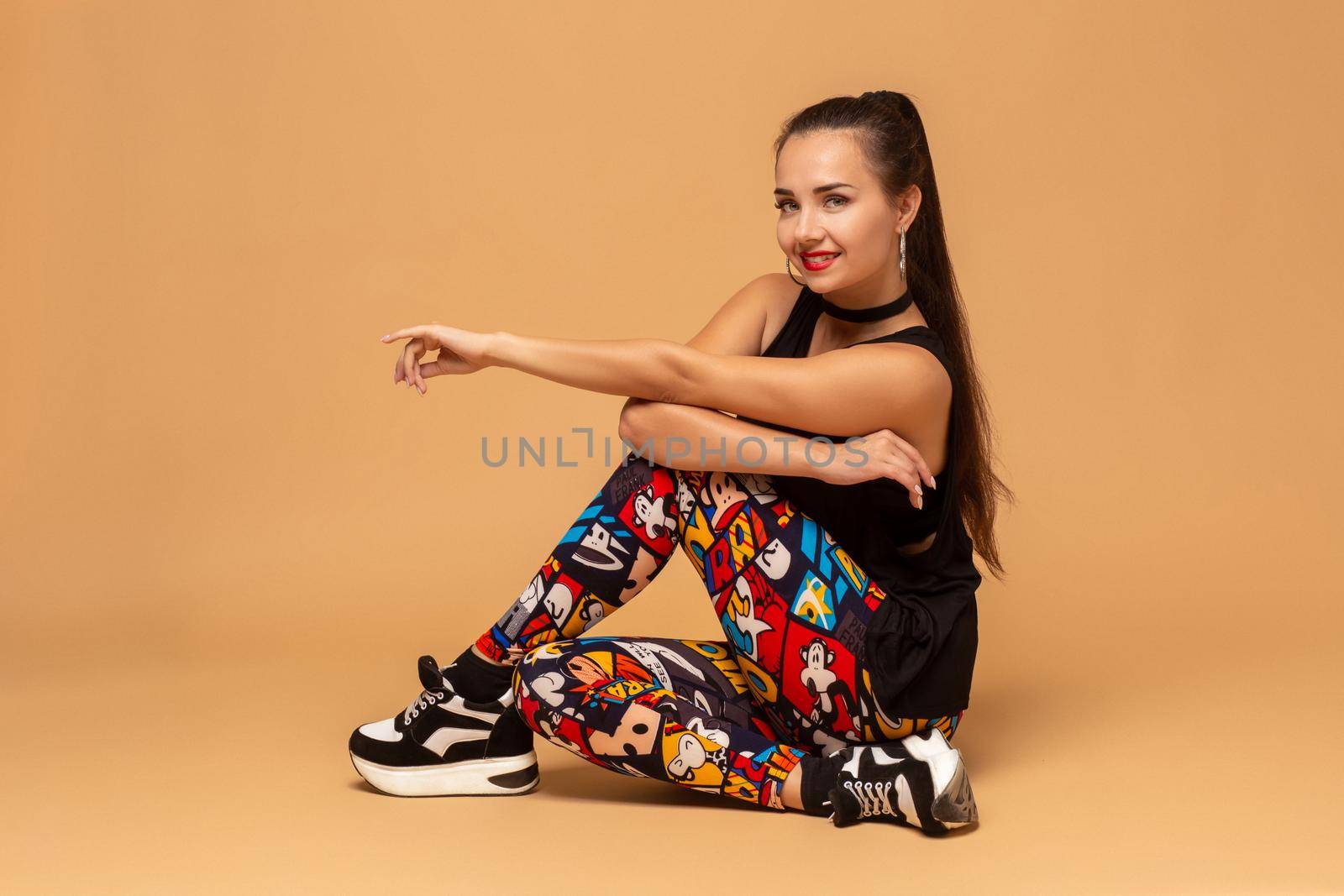 Young female dancer on studio background. Young modern style dancer girl sitting on floor in studio. Pretty female dancer of dancehall, jazz funk, hip hop